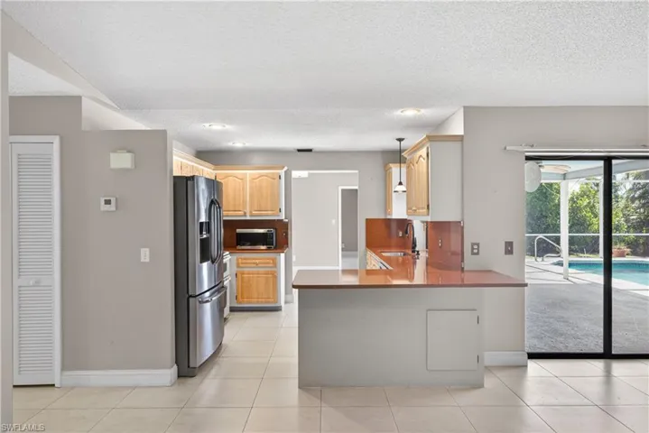 Kitchen featuring stainless steel appliances, wood cabinetry, a peninsula with a red-toned countertop, and recessed lighting