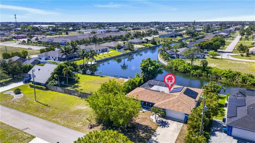 Waterfront property featuring a single-story residence with a brown shingle roof, solar panel installation, and an attached garage