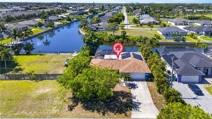Waterfront property featuring a screened lanai, solar panels, mature landscaping, and a concrete driveway