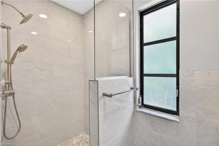 Walk-in shower featuring light-toned tilework, a dual shower head system, and a clear glass enclosure