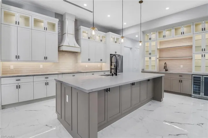 Kitchen with tasteful backsplash, a kitchen island with sink, custom exhaust hood, and light tile patterned floors