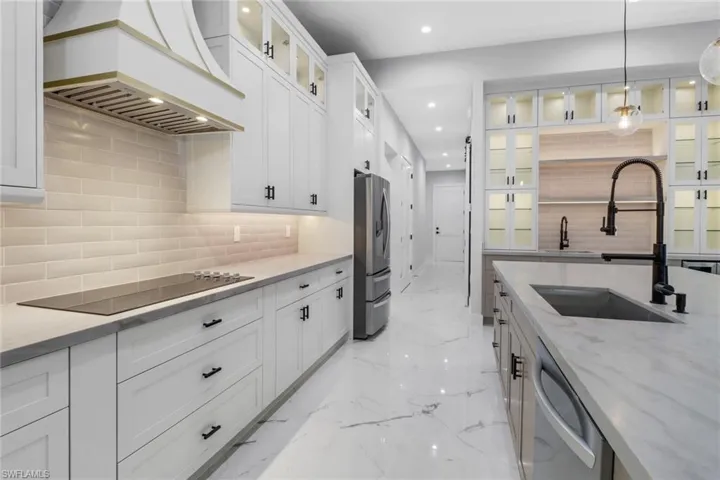 Kitchen featuring decorative backsplash, custom range hood, white cabinets, appliances with stainless steel finishes, and sink.