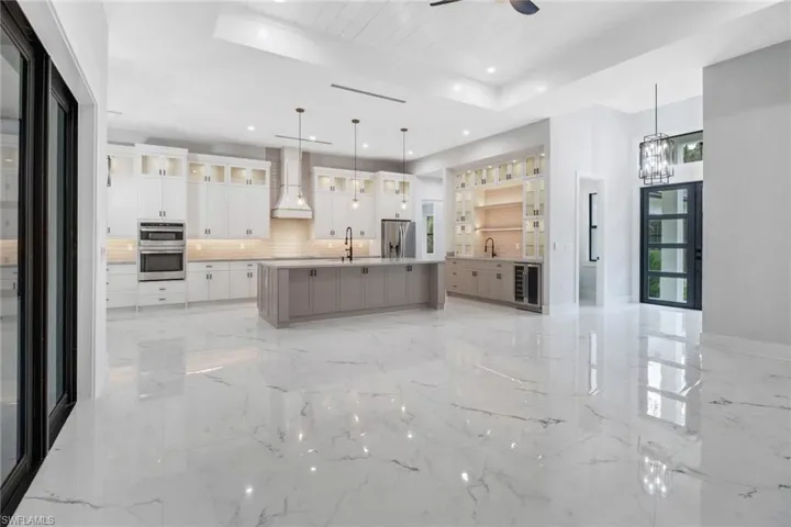Kitchen with appliances with stainless steel finishes, decorative light fixtures, a raised ceiling, a kitchen island with sink, and light tile patterned floors.