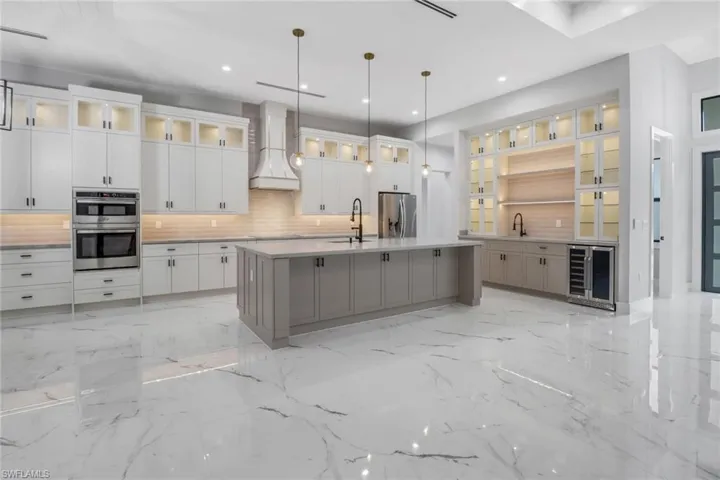 Kitchen featuring premium range hood, backsplash, hanging light fixtures, an island with sink, and wine cooler