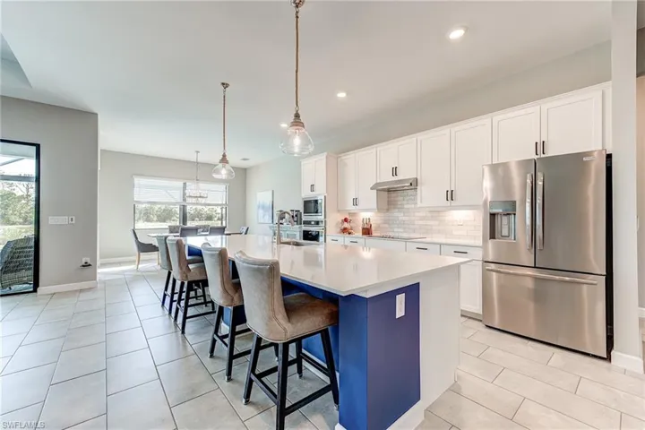Kitchen featuring an island with sink, under cabinet range hood, backsplash, stainless steel appliances, and light countertops