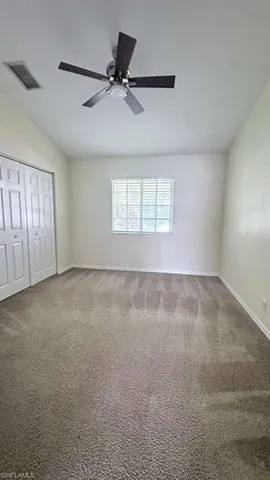 Carpeted room featuring a ceiling fan with dark wood-finish blades, a white window blind, and bi-fold closet doors