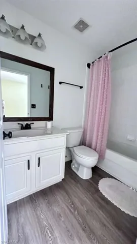 Bathroom featuring a white vanity with black hardware, a framed mirror, a three-light vanity fixture, a toilet, and wood-finish flooring
