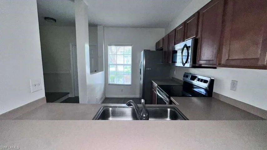 Kitchen featuring a double basin stainless steel sink, wood-finish cabinetry, a freestanding range, an over-the-range microwave, and a refrigerator