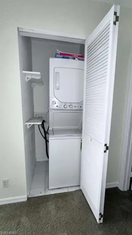 Dedicated laundry closet featuring a white stackable washer and dryer unit, white louvered bifold doors, and a tiled floor