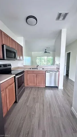 Kitchen featuring wood-finish flooring, stainless steel appliances, wood cabinetry, and a ceiling fan in the adjacent room