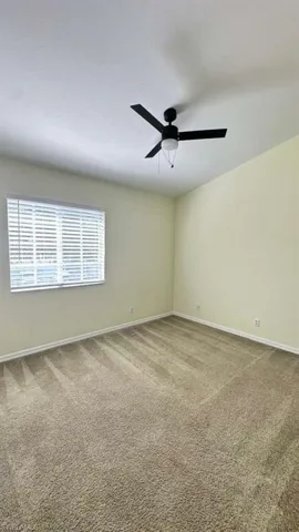 Spacious room featuring neutral carpeting, a window with horizontal blinds, and a ceiling fan with integrated lighting