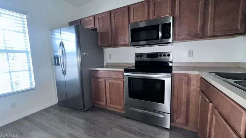 Kitchen featuring wood-finish flooring, stainless steel appliances, wood cabinetry, and a double-basin sink