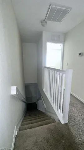 Carpeted staircase featuring white balusters and a wall-mounted handrail, with a flush-mount light fixture and ceiling vent visible overhead
