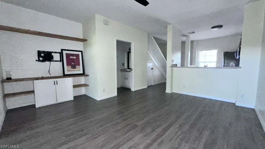 Spacious living area featuring wood-finish flooring, a ceiling fan, and built-in shelving with integrated cabinetry