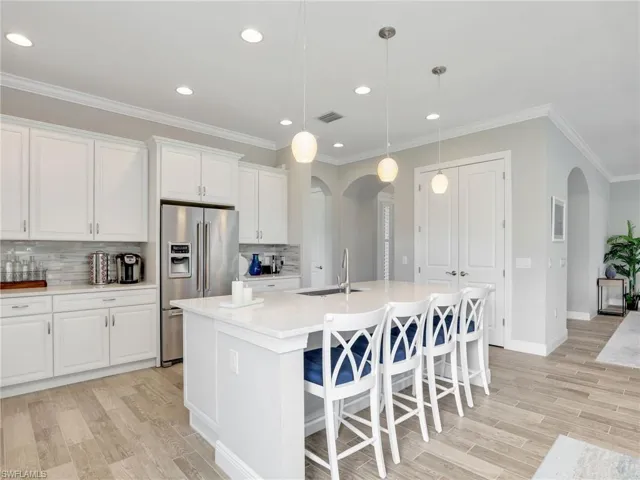 Kitchen featuring decorative backsplash, arched walkways, high end refrigerator, white cabinets, and ornamental molding
