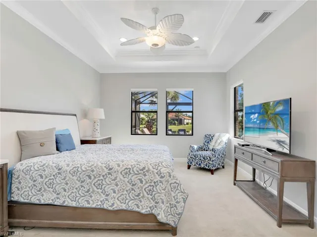 Bedroom with a tray ceiling, light carpet, ornamental molding, and ceiling fan