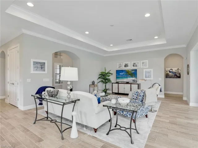 Living area featuring arched walkways, a tray ceiling, recessed lighting, ornamental molding, and wood tiled floors