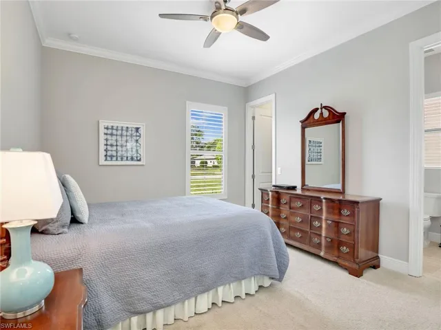 Bedroom with ornamental molding, light colored carpet, ceiling fan, and ensuite bath