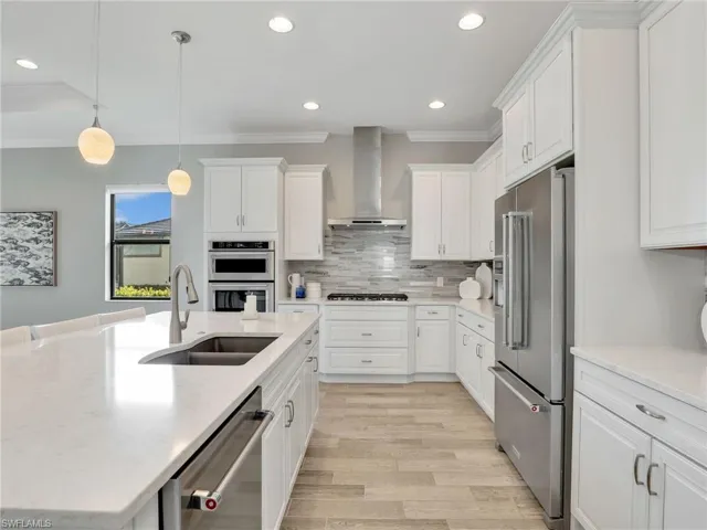 Kitchen with pendant lighting, light stone countertops, ornamental molding, recessed lighting, and white cabinets