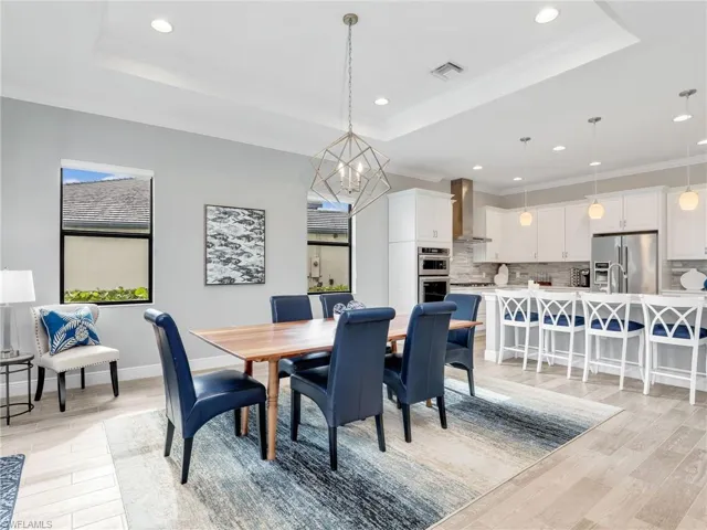 Dining space featuring a tray ceiling, crown molding, light wood-type flooring, a chandelier, and recessed lighting