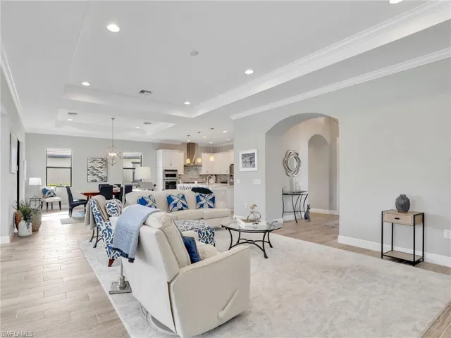 Living room with a raised ceiling, recessed lighting, light wood-style flooring, arched walkways, and crown molding