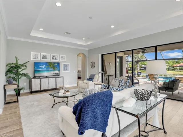 Living area with wood tiled floors, recessed lighting, a tray ceiling, arched walkways, and a sunroom