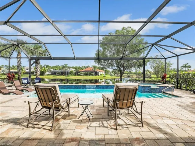 View of pool featuring a patio, a sunroom, a pool with connected hot tub, a water view, and glass enclosure