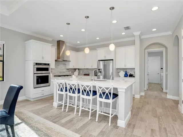 Kitchen with a kitchen breakfast bar, stainless steel appliances, ornamental molding, arched walkways, and a center island with sink