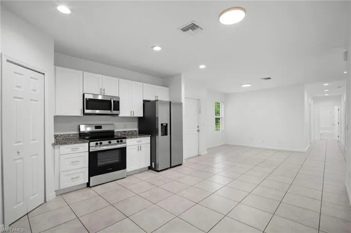 Kitchen featuring stainless steel appliances, white cabinetry, recessed lighting, light tile patterned floors, and dark stone countertops