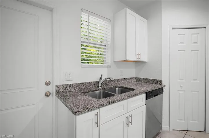 Kitchen with dark stone counters, white cabinetry, dishwasher, light tile patterned floors, and a textured wall