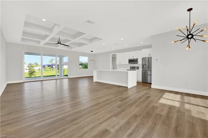 Unfurnished living room with coffered ceiling, ceiling fan with notable chandelier, hardwood / wood-style floors, beamed ceiling, and sink