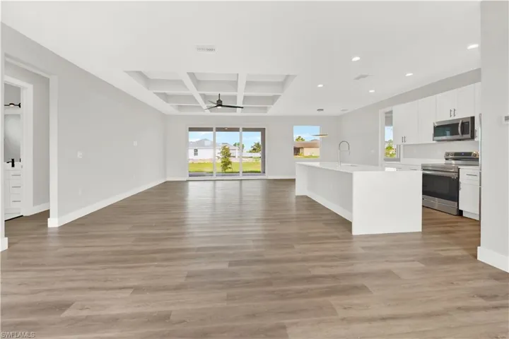 Kitchen with ceiling fan, stainless steel appliances, wood-type flooring, coffered ceiling, and a kitchen island with sink