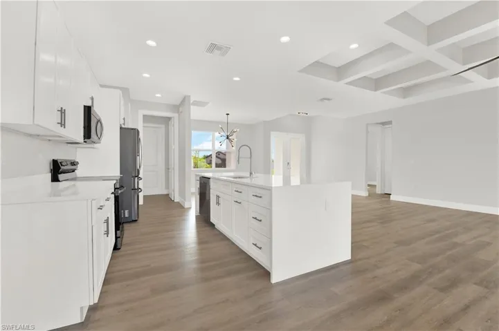Kitchen featuring coffered ceiling, a center island with sink, wood-type flooring, white cabinets, and appliances with stainless steel finishes