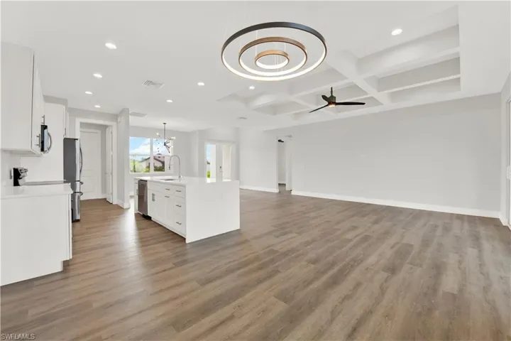 Kitchen featuring coffered ceiling, ceiling fan with notable chandelier, hardwood / wood-style floors, an island with sink, and appliances with stainless steel finishes