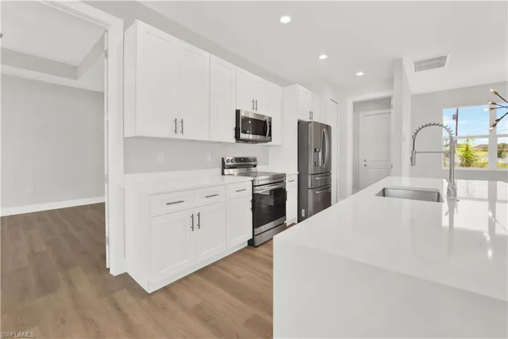 Kitchen featuring stainless steel appliances, a notable chandelier, hardwood / wood-style floors, white cabinets, and sink