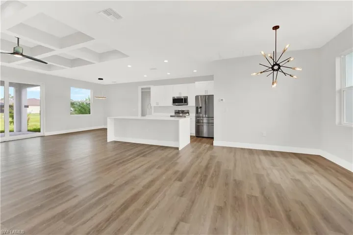 Unfurnished living room with coffered ceiling, ceiling fan with notable chandelier, light wood-type flooring, and beam ceiling