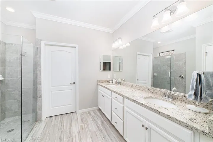 Primary bath, dual sinks in vanity, glass shower enclosure, linen closet and custom walk-in closet are featured.