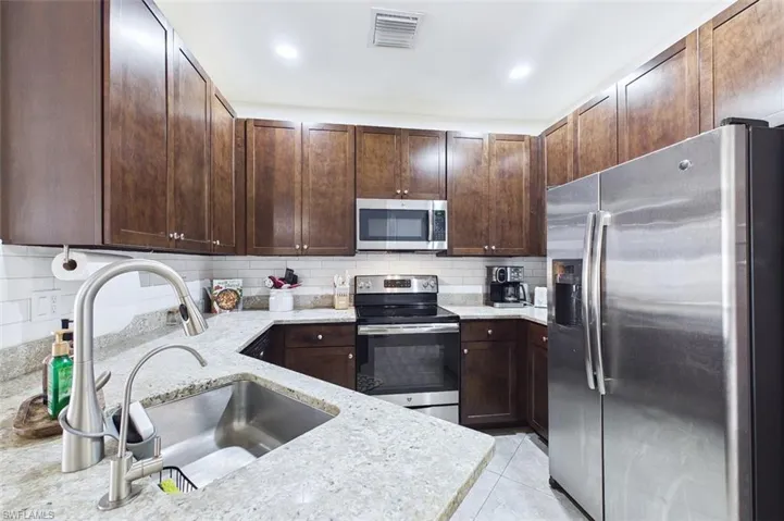 Kitchen featuring stainless steel appliances, tasteful backsplash, light stone counters, and dark brown cabinetry