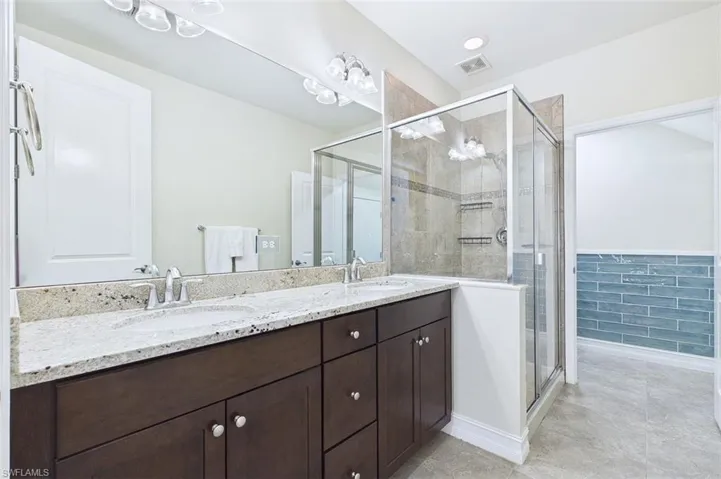 Full bath featuring double vanity, a shower stall, a wainscoted wall, and light tile patterned floors