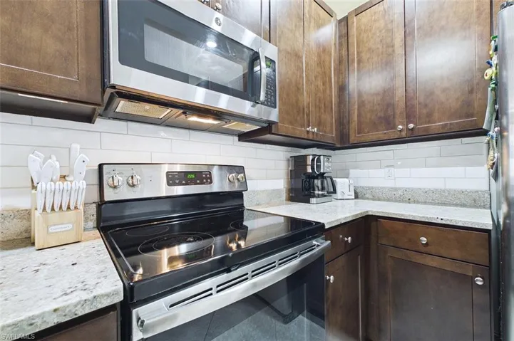 Kitchen with appliances with stainless steel finishes, light stone countertops, dark brown cabinets, and backsplash