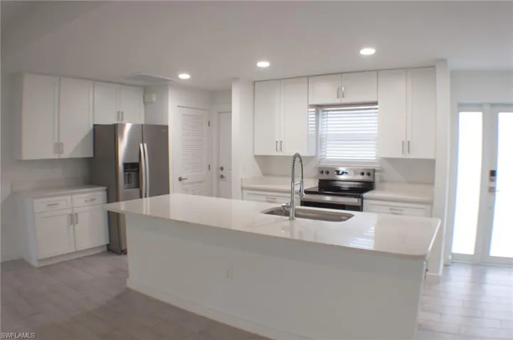 Spacious kitchen featuring an island with an undermount sink, white cabinetry with silver-tone hardware, stainless steel appliances, light-toned countertops, and wood-finish flooring