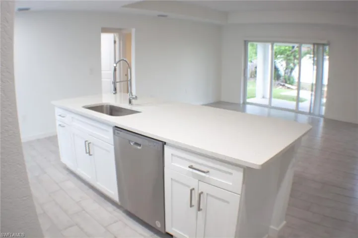 Kitchen island with white shaker cabinetry, an undermount stainless steel sink, a gooseneck faucet, and a stainless steel dishwasher