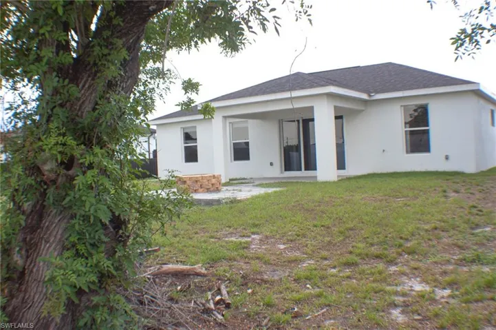 Rear exterior featuring a white stucco finish, dark shingle roof, and a covered patio with sliding glass doors