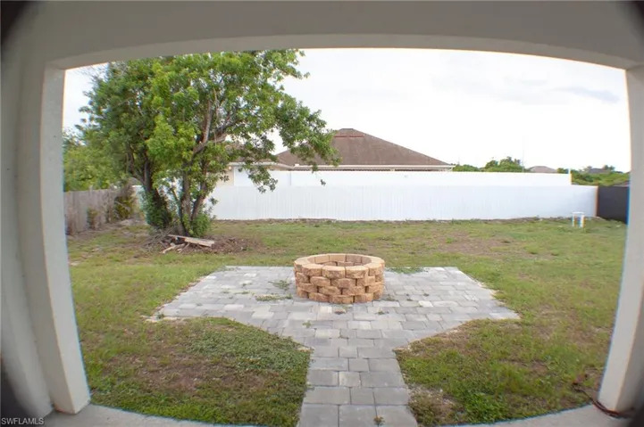 Private backyard featuring a paver patio with a built-in stone fire pit, mature tree, and full perimeter fencing