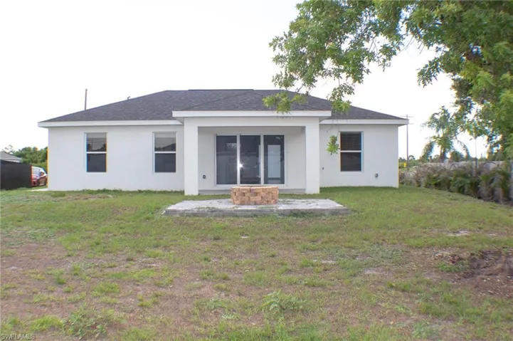 Rear exterior featuring a covered patio with sliding glass doors, white stucco finish, and a dark shingle roof