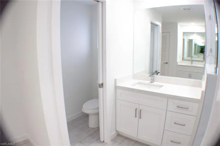 White vanity with integrated sink, stone countertop, brushed nickel hardware, and a frameless wall mirror