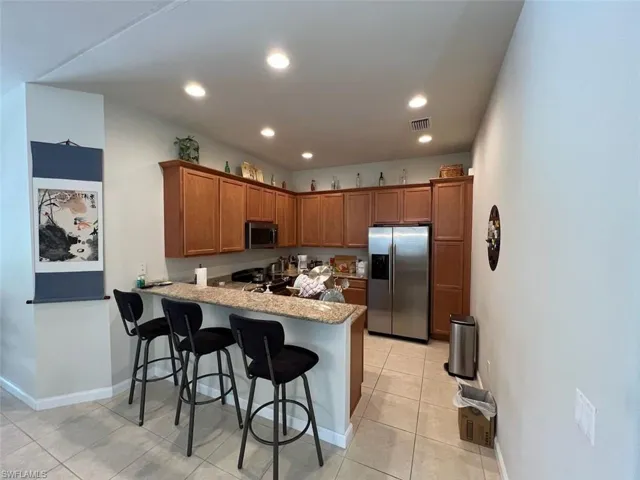 Kitchen with light tile patterned flooring, appliances with stainless steel finishes, kitchen peninsula, and a breakfast bar