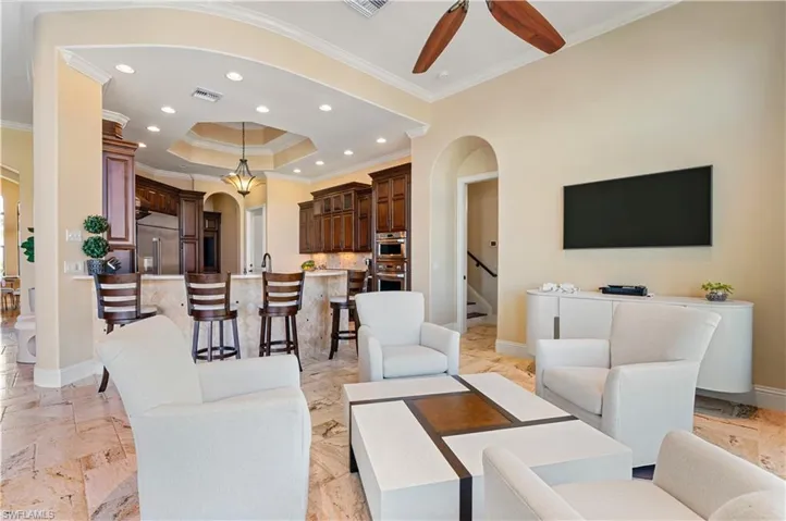 Living room with arched walkways, a tray ceiling, recessed lighting, ornamental molding, and ceiling fan