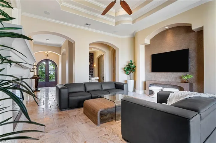 Living room featuring crown molding, stone tile flooring, a raised ceiling, arched walkways, and a ceiling fan