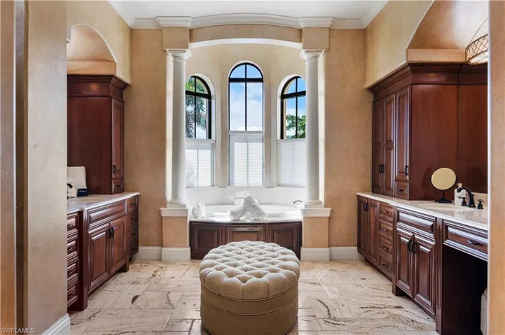 Bathroom with decorative columns, two vanities, crown molding, and a bath